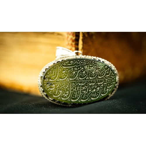 8 - AN OVAL FORM SILVER FRAMED GREEN JADE PENDANT Of oval form, two lines of Arabic inscription engraved... 