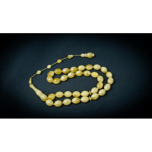 65 - AN AMBER PRAYER BEADS, 20TH CENTURY, The tasbih strung  with 33  ovoid  beads, flat stops, narrowing... 