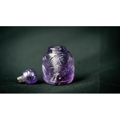 73 - A MUGHAL STYLE PURPLE CARVED CRYSTAL SCENE BOTTLE WITH LID, Rising from a 
triangle base, three side... 