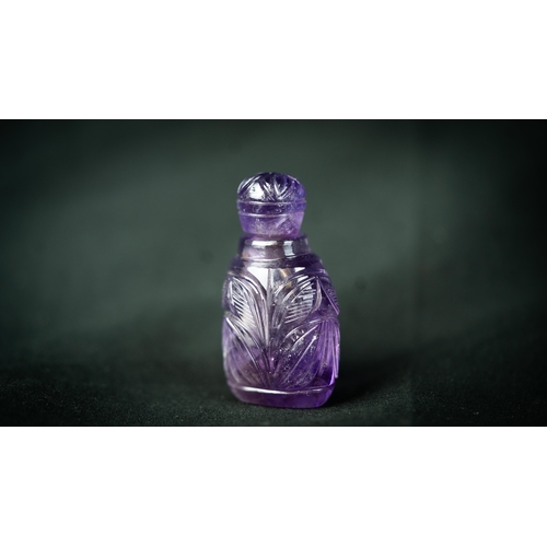 73 - A MUGHAL STYLE PURPLE CARVED CRYSTAL SCENE BOTTLE WITH LID, Rising from a 
triangle base, three side... 