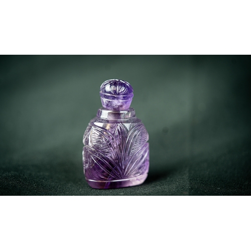 73 - A MUGHAL STYLE PURPLE CARVED CRYSTAL SCENE BOTTLE WITH LID, Rising from a 
triangle base, three side... 