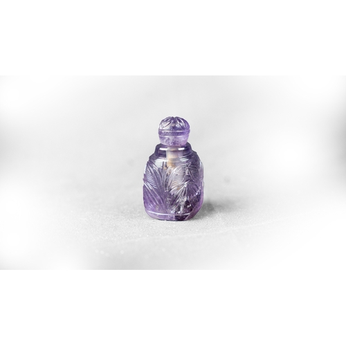 73 - A MUGHAL STYLE PURPLE CARVED CRYSTAL SCENE BOTTLE WITH LID, Rising from a 
triangle base, three side... 