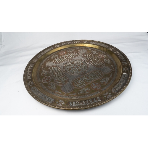 76 - A SILVER-INLAID BRASS TRAY
Of large circular form, resting on a flat, plain base, rising to a flatte... 