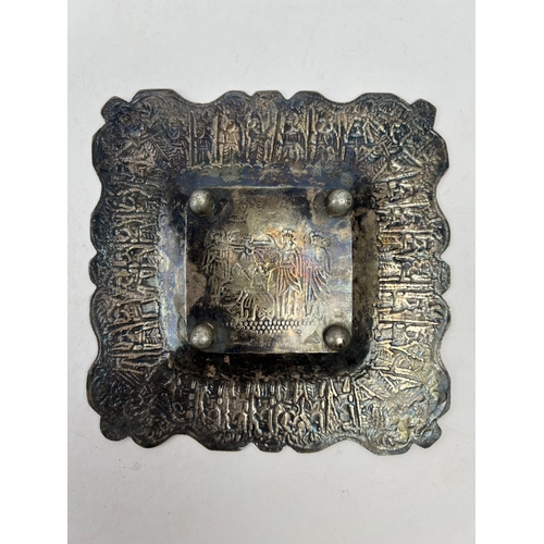 64 - A QAJAR SILVER PLATE, 

Of square form, resting on four bulbous feet, with repoussé and chased decor... 