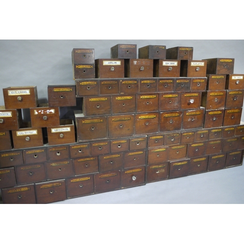 83 - A run of 54 graduated pharmacy drawers in three sections mahogany stained and lettered in black on g... 