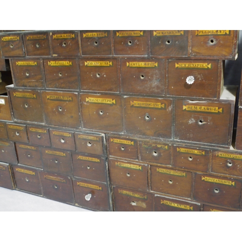 83 - A run of 54 graduated pharmacy drawers in three sections mahogany stained and lettered in black on g... 