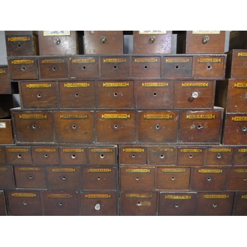 83 - A run of 54 graduated pharmacy drawers in three sections mahogany stained and lettered in black on g... 