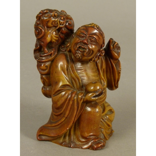 101 - A CHINESE SOAPSTONE FIGURE of a seated figure his left arm raised, he holds a fruit in his right han... 