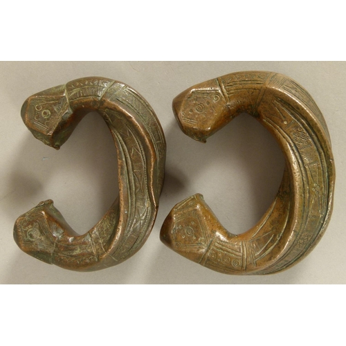 125 - A PAIR OF BRONZE PENANNULAR BRACELETS each with square faceted terminals, bands of geometric decorat... 