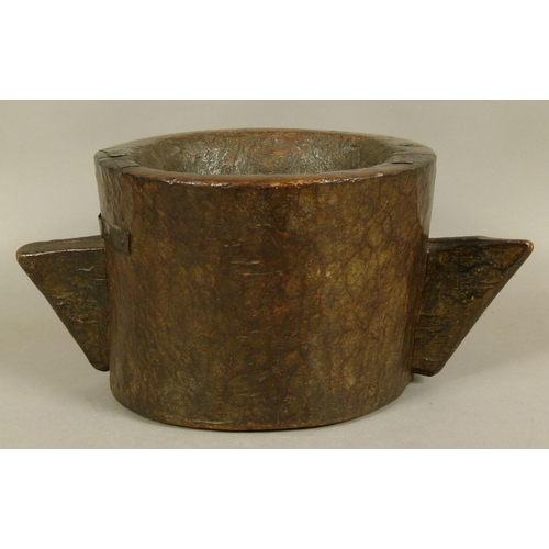 558 - AN 18TH CENTURY TWO HANDLED WOODEN MORTAR of chip-carved cylindrical trunk form with angular handles... 