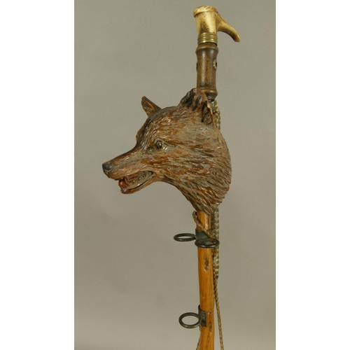 574 - A CARVED TREEN FOX MASK MOUNTED RIDING CROP PIPE RACK with antler handle, 50cm long