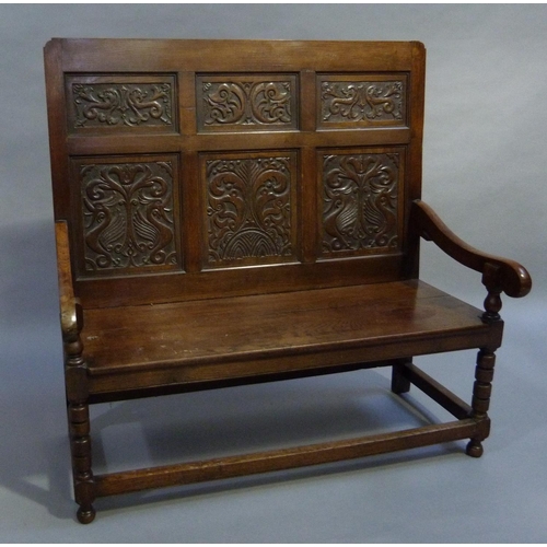 285 - An Oak settle the raised back having six carved panels, slab arms, planked seat and on turned uprigh... 