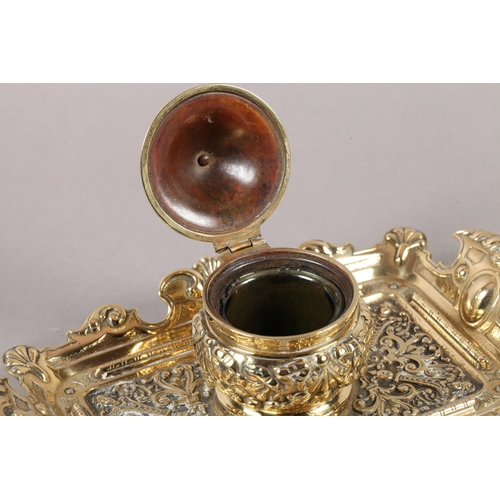 14 - A Victorian brass desk standish fitted with a central inkwell and cover cast with ribboned harebells... 