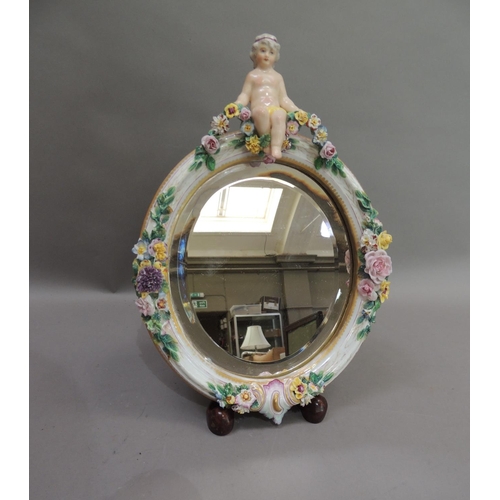 55 - A Continental porcelain floral encrusted oval mirror, the bevel plate within a frame set to the top ... 