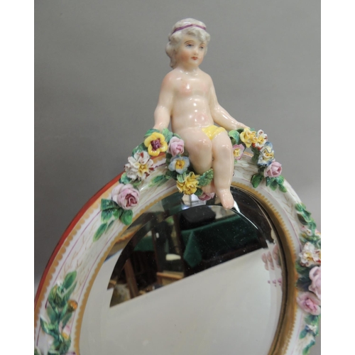 55 - A Continental porcelain floral encrusted oval mirror, the bevel plate within a frame set to the top ... 