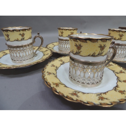 12 - A set of four Aynsley porcelain coffee cans and saucers, the cans set within pierced silver cylindri... 