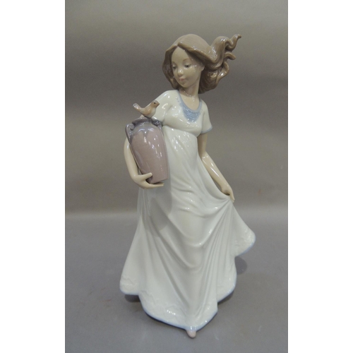 52 - A Nao porcelain figure of a young girl carrying a two handled vase under her arm with a bird perched... 