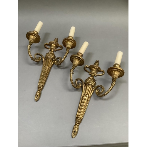 52 - A pair of gilt metal twin light wall sconces of classical design, two handled urn finial and leaf ca... 