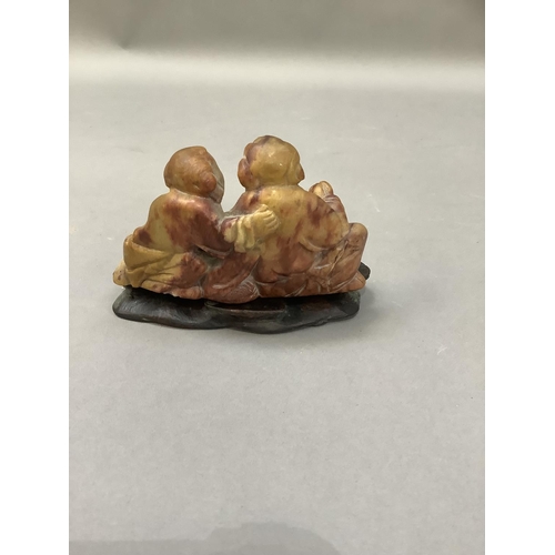 54 - A carved soapstone figure group of a female offering peaches to a corpulent figure on hardwood stand... 