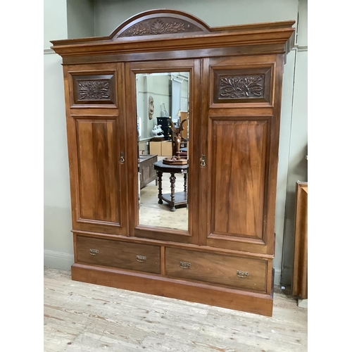 405 - A late Victorian walnut wardrobe having an arch pediment, above a mirror door to the centre flanked ... 