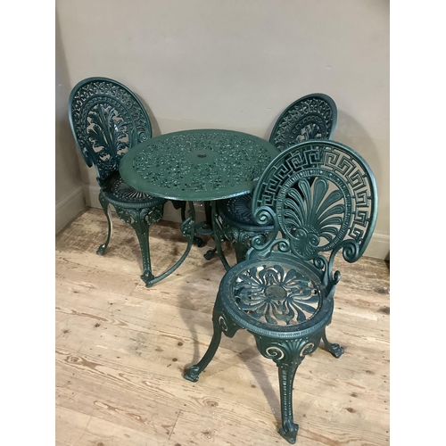 321 - A patio table of circular outline and pierced foliate design together with three green metal chairs ... 