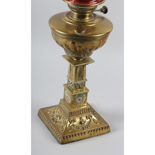 37 - A VICTORIAN BRASS OIL LAMP HAVING A CRANBERRY GLASS SHADE, writhen embossed reservoir above a square... 