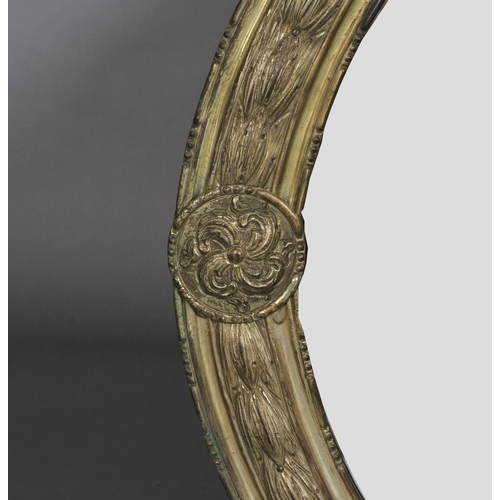 569 - A LATE 19TH CENTURY GILT METAL FRAMED OVAL WALL MIRROR, the frame embossed with band of harebells wi... 