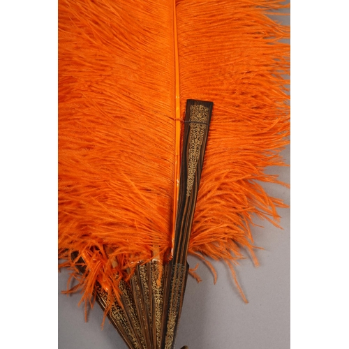 101 - An orange ostrich feather fan, the monture of patterned wood, the guards decorated in gold, overall ... 