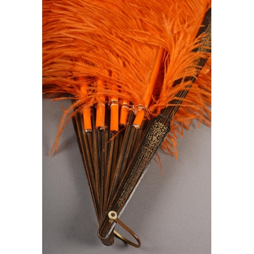 101 - An orange ostrich feather fan, the monture of patterned wood, the guards decorated in gold, overall ... 