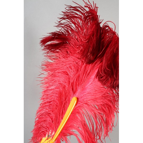 107 - A shaded cerise ostrich feather fan, 1920’s the curled feathers mounted on butterscotch yellow plast... 