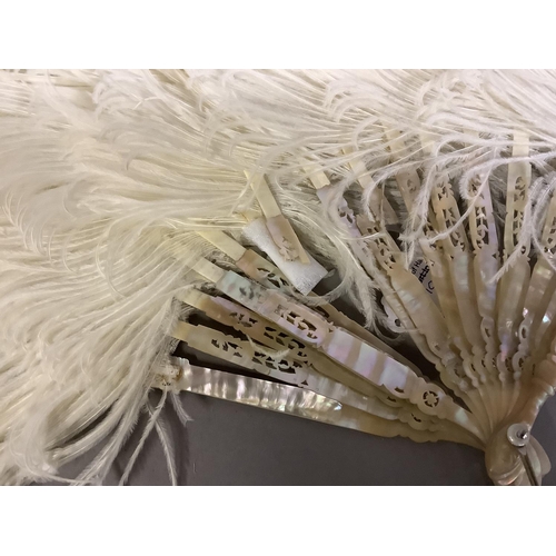 104 - An attractive white ostrich feather fan, being mounted on pink mother of pearl the sticks carved, sh... 