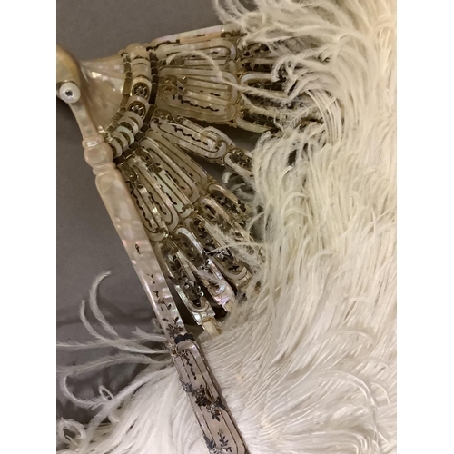 104 - An attractive white ostrich feather fan, being mounted on pink mother of pearl the sticks carved, sh... 