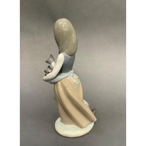 15 - A Lladro figure of a girl holding kittens in her apron, a cat at her feet, 25cm high