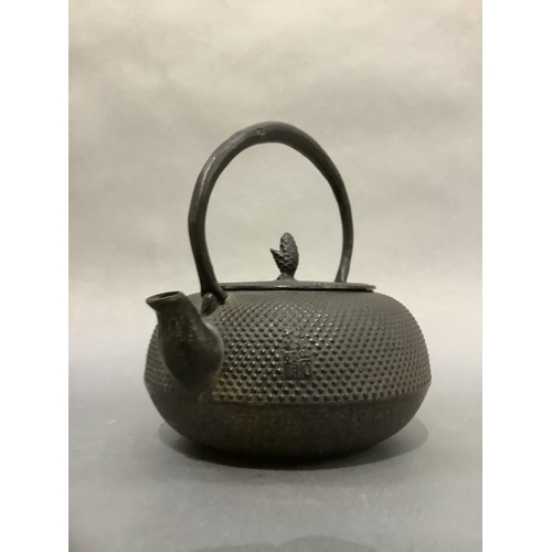 52 - A Japanese black iron teapot of compressed circular form with disc lid and pine cone finial, raised ... 