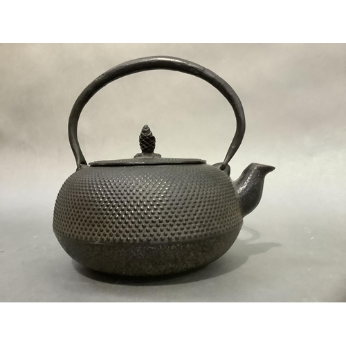 52 - A Japanese black iron teapot of compressed circular form with disc lid and pine cone finial, raised ... 