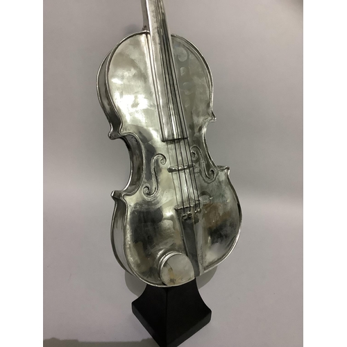 18 - A white metal violin raised on an ebonised pedestal,62cm high