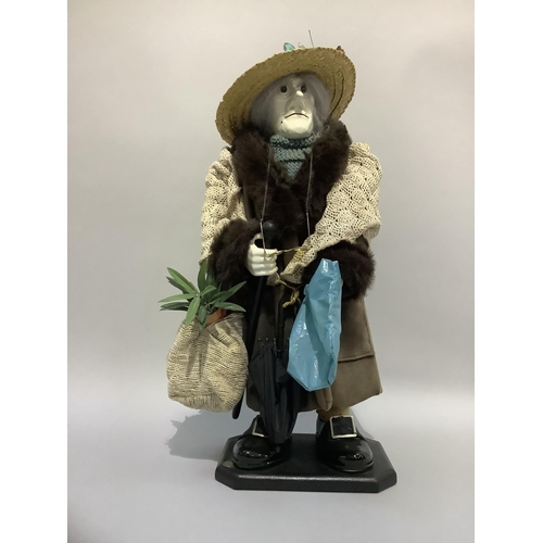 23 - A figure of an elderly woman wearing a straw hat, faux fur coat with shawl carrying umbrella and var... 