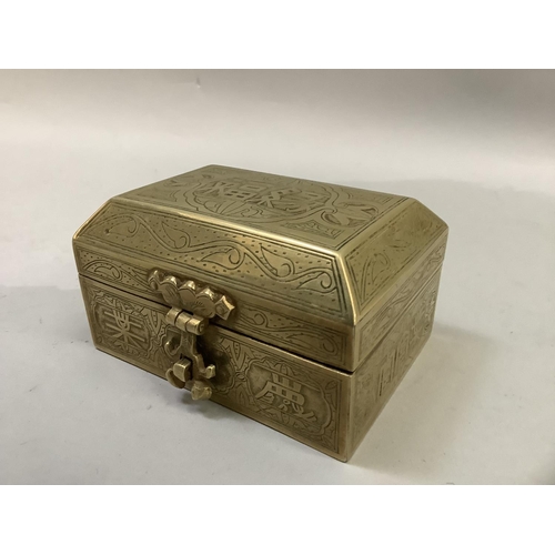 63 - A Chinese brass box having a canted lid with strapwork hinges and lock all over engraved with charac... 