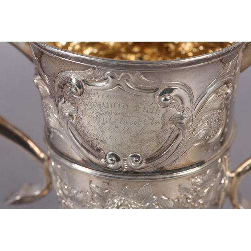 194 - A GEORGE III SILVER TROPHY CUP with rose chasing, banded with foliate c-scroll handles, later engrav... 