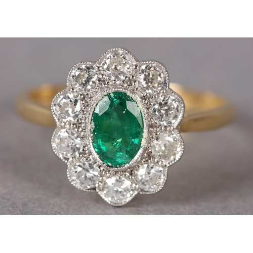 306 - AN EMERALD AND DIAMOND CLUSTER RING, the oval faceted emerald millegrain set within a surround of br... 