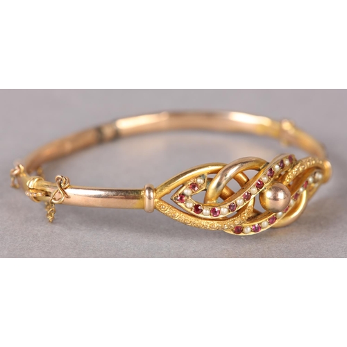 330 - A VICTORIAN GARNET AND SEED PEARL STIFF HINGED BANGLE in 9ct gold, the writhen knot, polished stone ... 