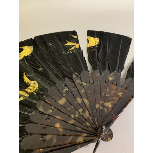 113 - A late 19th century black feather fan, the monture of tortoiseshell, the feathers painted in gold wi... 