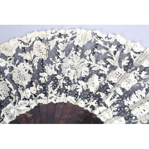 85 - c1905, a black net and mixed Brussels lace fan, the unusual needle lace floral motifs applied to bla... 