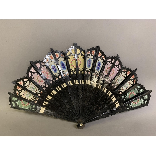 16 - Two unusual 20th century fans, the first a wood brisé painted black, the sticks shaped and pierced, ... 