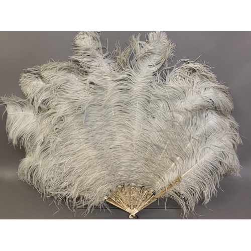 109 - A large white ostrich feather fan, the bone sticks carved, pierced and coloured in several shades of... 