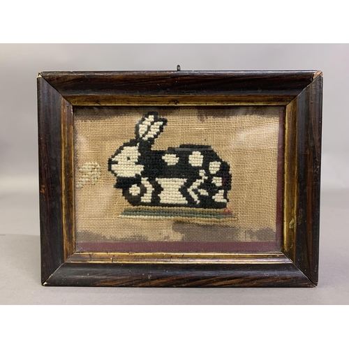 154 - A charming, naïve woolwork picture of a rabbit, seated on a grassy bank, black and white on canvas, ... 