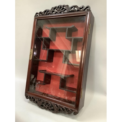 161 - An Oriental hardwood and glazed hanging display cabinet with pierced pediment and apron