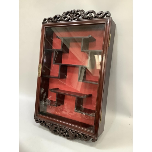 161 - An Oriental hardwood and glazed hanging display cabinet with pierced pediment and apron