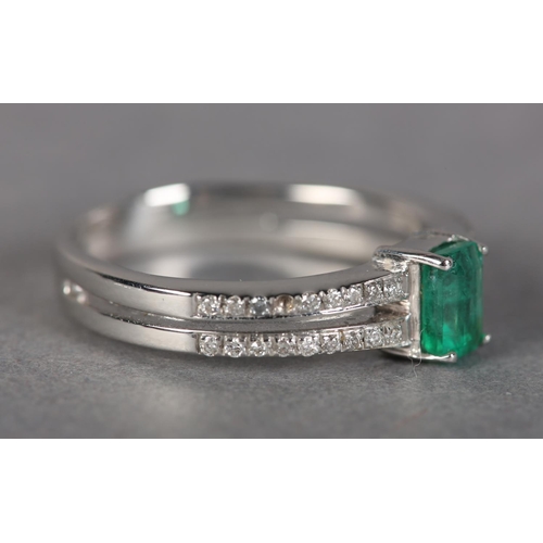 185 - AN EMERALD AND DIAMOND RING IN 18CT WHITE GOLD, claw set to the centre with a step cut emerald flank... 