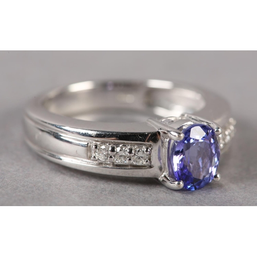 174 - A TANZANITE AND DIAMOND RING in 18ct white gold by Iliana, claw set to the centre with an oval facet... 